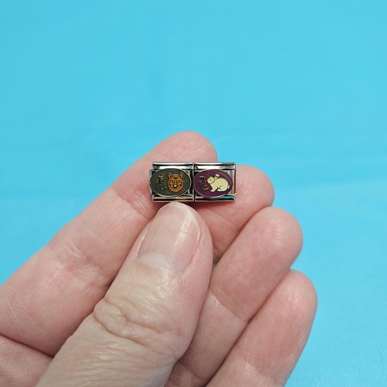 May include: Two silver charm bracelets with animal designs. The left charm features a brown bear with a yellow background. The right charm features a white rabbit with a purple background.