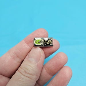 May include: Two silver charm bracelet links with a black and white horse design and a green and white horse design.