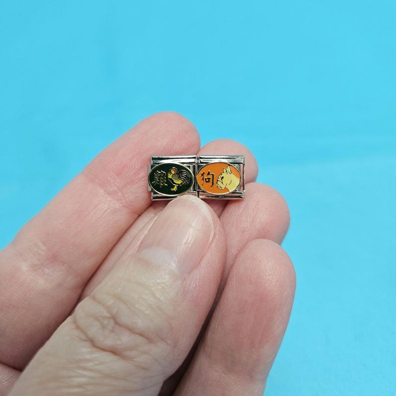 May include: Two silver charm bracelets with Chinese zodiac symbols. The left charm features a rooster with the Chinese character for rooster. The right charm features a dog with the Chinese character for dog.