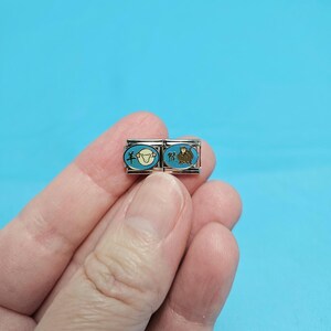 May include: Two silver charm bracelets with blue enamel and Chinese characters. The left charm features a white sheep with the character "羊" for "sheep" and the right charm features a brown monkey with the character "猴" for "monkey".