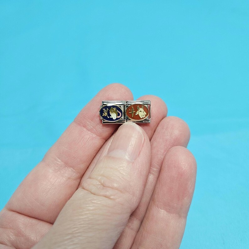 May include: Two silver charm bracelets with enamel Chinese zodiac symbols. The left charm is blue with a rat and the right charm is orange with an ox.