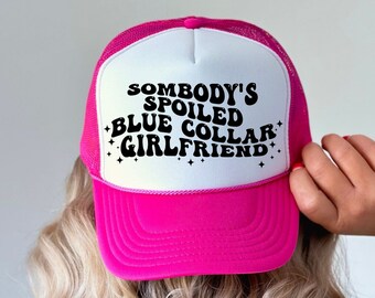 Può includere: Cappellino da camionista rosa e bianco con il testo "Somebody's Spoiled Blue Collar Girlfriend" in nero.