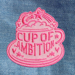 May include: Pink embroidered iron-on patch featuring a cup of coffee and the text "Cup of Ambition".