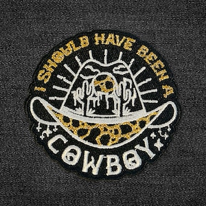 May include: Black and gold embroidered patch featuring a cowboy hat and the text "I should have been a cowboy".
