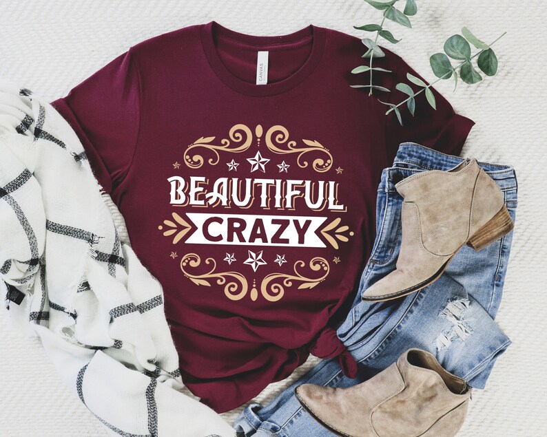 Pu&ograve; includere: Maglietta color borgogna con un design oro e bianco che dice "Beautiful Crazy".
