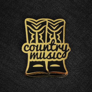 May include: Gold-coloured pin with a black outline of two cowboy boots and the text "country music".