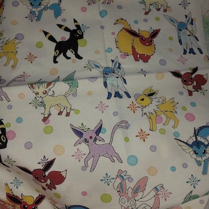 Puede incluir: Tela blanca con un patrón repetido de personajes de Pokémon coloridos. Los personajes incluyen Eevee, Vaporeon, Jolteon, Flareon, Espeon, Umbreon, Glaceon, Leafeon, Sylveon y otros.