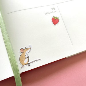 May include: A brown mouse sticker with a white background. The mouse is standing on its hind legs with its front paws together. The mouse is looking to the right.