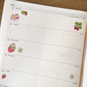 May include: A weekly planner with a June calendar and stickers of strawberries, a mouse, and a flower. The planner has a white background with black lines and numbers.