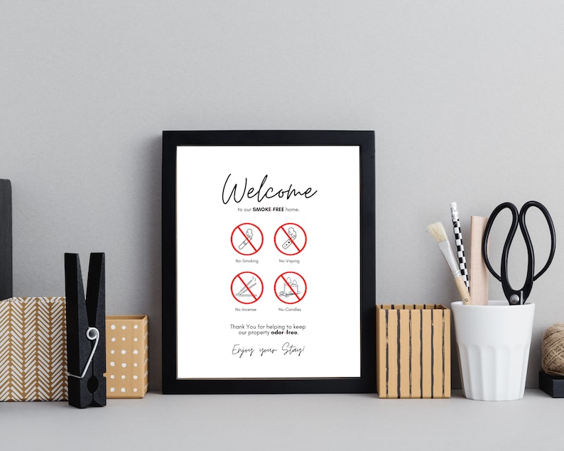 Op de afbeelding: Een ingelijst bord met een zwarte rand toont de woorden "Welcome" en "to our SMOKE FREE home." Hieronder staan vier rode en zwarte verbodssymbolen voor roken, vapen, wierook en kaarsen. Het bord bevat ook de tekst "Thank You for helping to keep our property odor-free. Enjoy your Stay!"