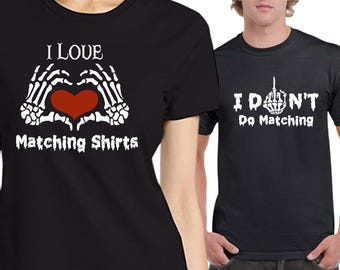 May include: Two black short-sleeve t-shirts. The first shirt features white skeleton hands forming a heart shape around a red heart with the text I LOVE Matching Shirts. The second shirt features a white skeleton hand giving the middle finger with the text I DON'T Do Matching.