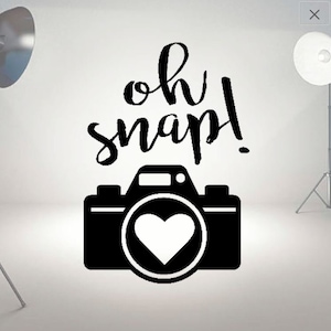 May include: Black and white graphic of a camera with a heart in the lens and the text "oh snap!" above it.