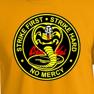 May include: Black and yellow Cobra Kai logo with a cobra snake, the words "Strike First Strike Hard No Mercy" and the words "Cobra Kai" in red.