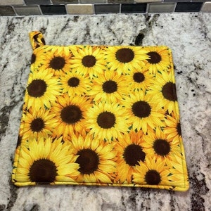 May include: A yellow and brown pot holder with a sunflower pattern.