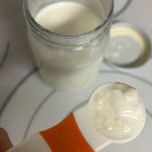 May include: A white measuring spoon filled with a thick, creamy white substance. The spoon is orange and white and has a number "1" on the side.