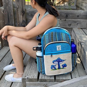 May include: A blue and black hemp backpack with a mushroom design and the text "Marijuana Hemp" on the front. The backpack has a zippered pocket and a mesh pocket on the side.