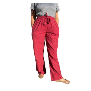 Könnte beinhalten: Rote Hose mit Kordelzugbund und Taschen. Die Hose hat eine lockere Passform und ein leicht ausgestelltes Bein. Der Stoff scheint ein strukturiertes Gewebe zu sein.