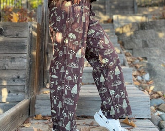 May include: Brown wide-leg trousers with a mushroom print. The trousers are worn with white clogs.