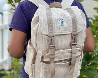 May include: A beige hemp backpack with a brown chevron pattern and adjustable straps. The backpack has a zippered pocket on the front and a small patch with the text "HIMALAYAN HEMP" and a leaf design.