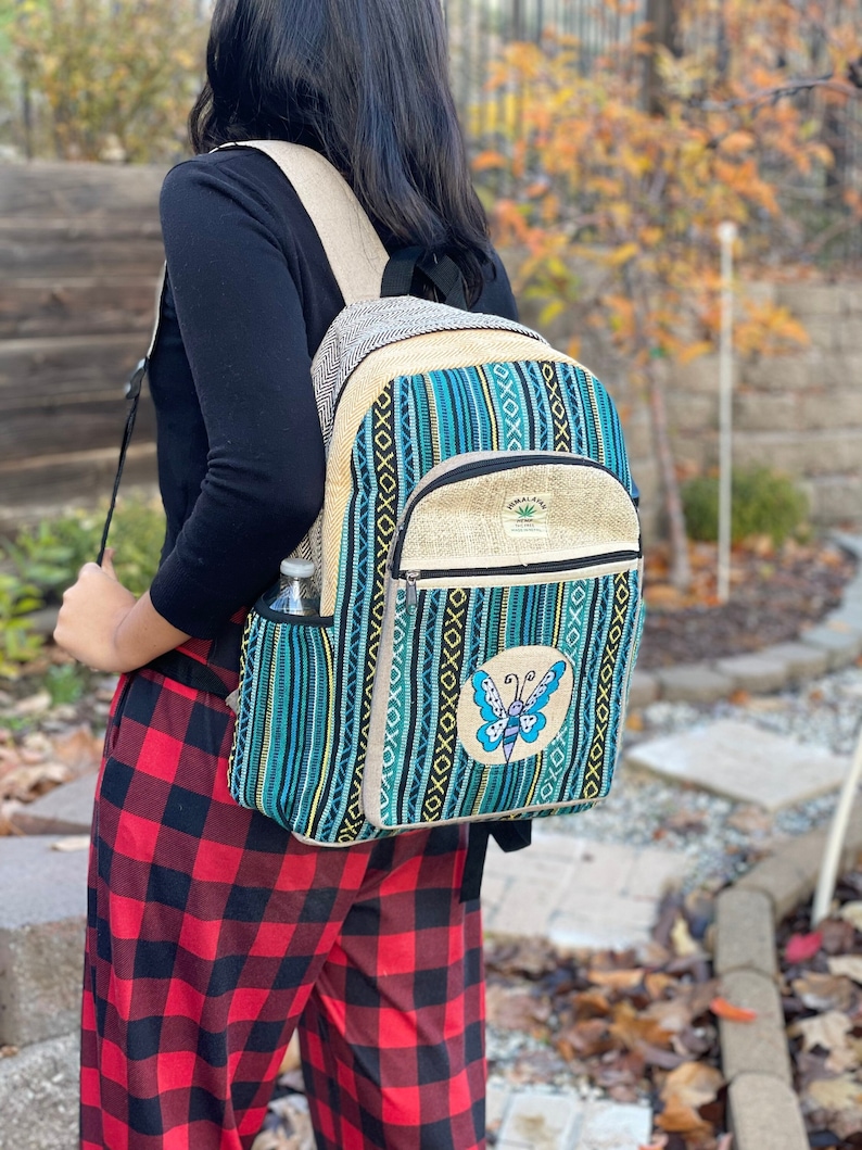 May include: A blue and green striped hemp backpack with a butterfly design and a small pocket on the front. The backpack has a hemp leaf logo that says "Himalayan Hemp".