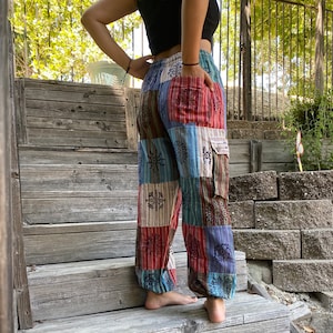 May include: Patchwork pants with a multi-colored design featuring geometric shapes and snowflakes. The pants have a cargo pocket on the right leg.