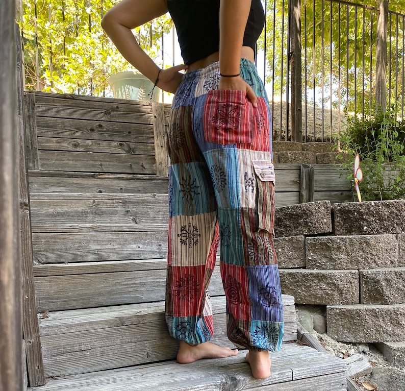 May include: Patchwork pants with a multi-colored design featuring geometric shapes and snowflakes. The pants have a cargo pocket on the right leg.