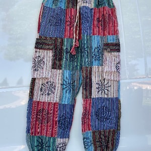 May include: Patchwork pants with a drawstring waist and side pockets. The pants are made of a variety of fabrics in shades of blue, red, green, and brown. The fabric is patterned with embroidered flowers and other designs.