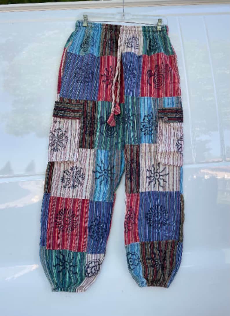 May include: Patchwork pants with a drawstring waist and side pockets. The pants are made of a variety of fabrics in shades of blue, red, green, and brown. The fabric is patterned with embroidered flowers and other designs.