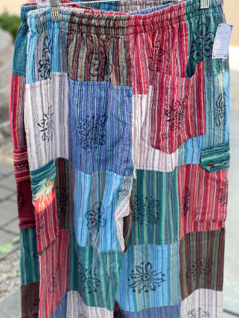 May include: Patchwork pants with a colorful striped pattern and floral designs. The pants have a drawstring waist and pockets.