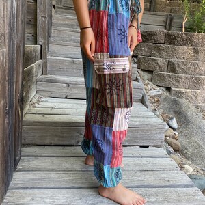 May include: Patchwork pants with a colorful, geometric pattern. The pants have a drawstring waist and a large cargo pocket on the left leg.