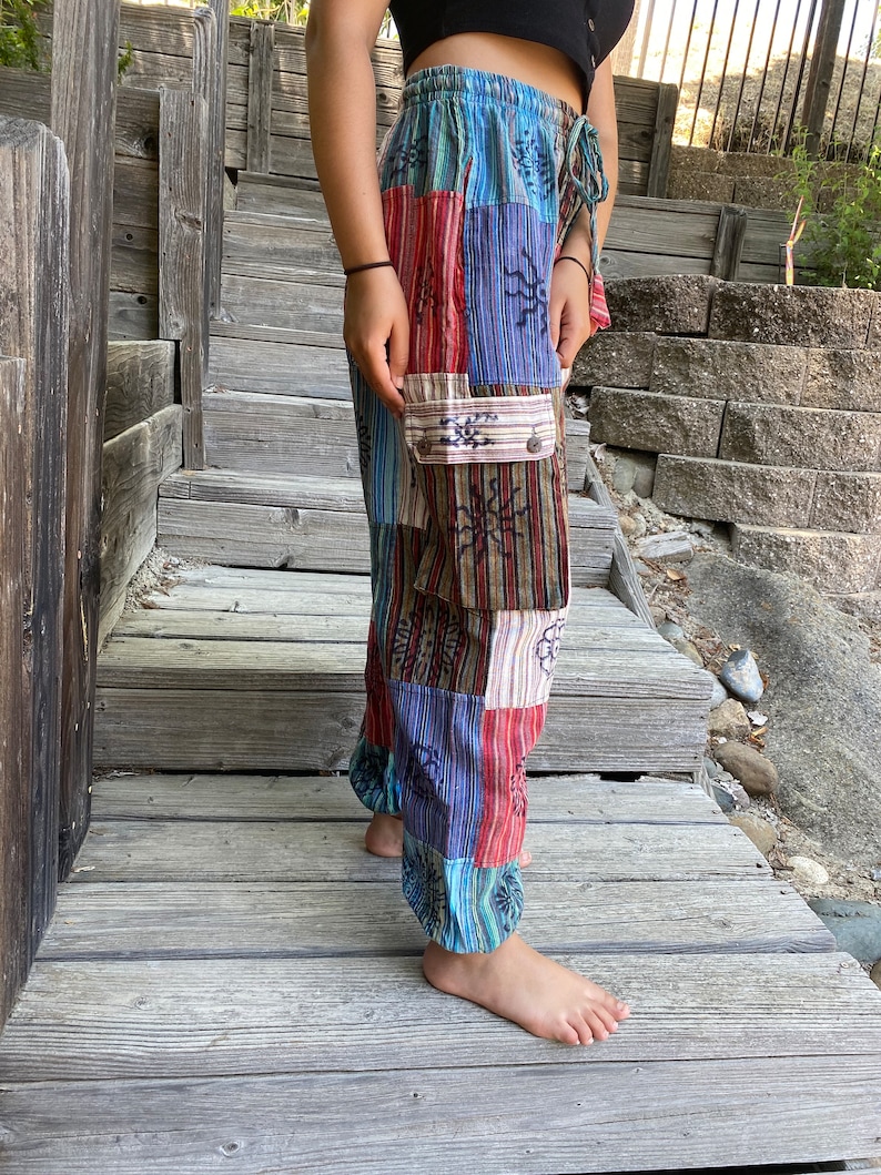 May include: Patchwork pants with a colorful, geometric pattern. The pants have a drawstring waist and a large cargo pocket on the left leg.