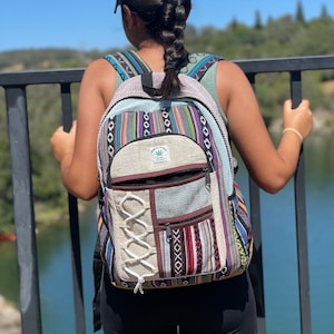 May include: A colorful backpack with a patchwork design. The backpack features a variety of patterns, including stripes, geometric shapes, and a cream-colored section with a crisscross design. The backpack has multiple pockets and adjustable straps. The text "Himalayan" is visible on the front.