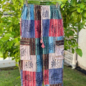 May include: Multicolored patchwork pants with a drawstring waist and side pockets. The pants feature a variety of floral and geometric patterns in shades of blue, red, green, and white.