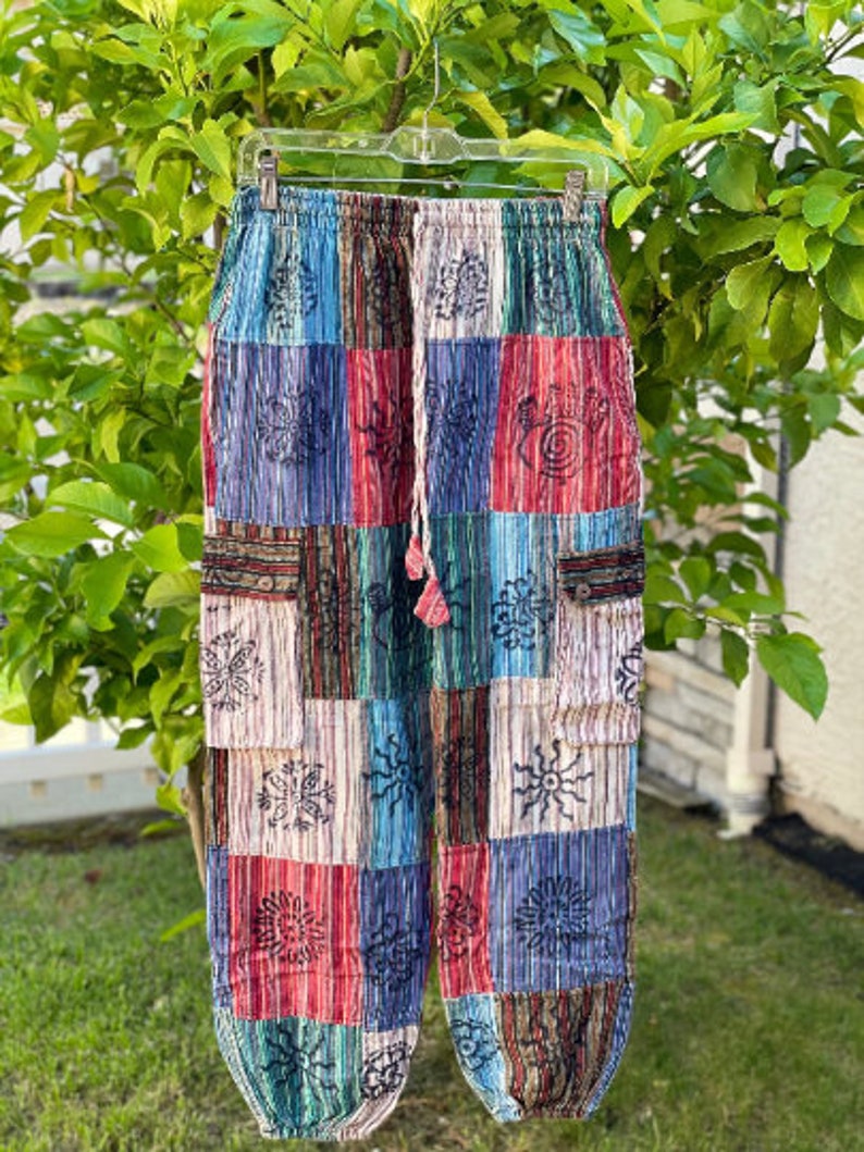 May include: Multicolored patchwork pants with a drawstring waist and side pockets. The pants feature a variety of floral and geometric patterns in shades of blue, red, green, and white.