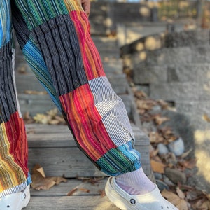 May include: A pair of colorful patchwork pants with a striped pattern. The pants are cuffed at the ankles and are being worn with white clogs.
