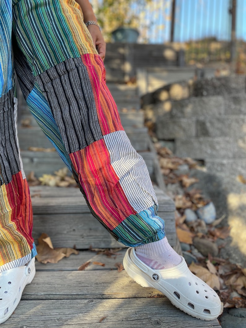 May include: A pair of colorful patchwork pants with a striped pattern. The pants are cuffed at the ankles and are being worn with white clogs.