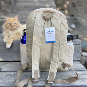 May include: A beige canvas backpack with adjustable straps. The backpack has a mesh pocket on the side and a tag that says "L&S International" and "MD-260".