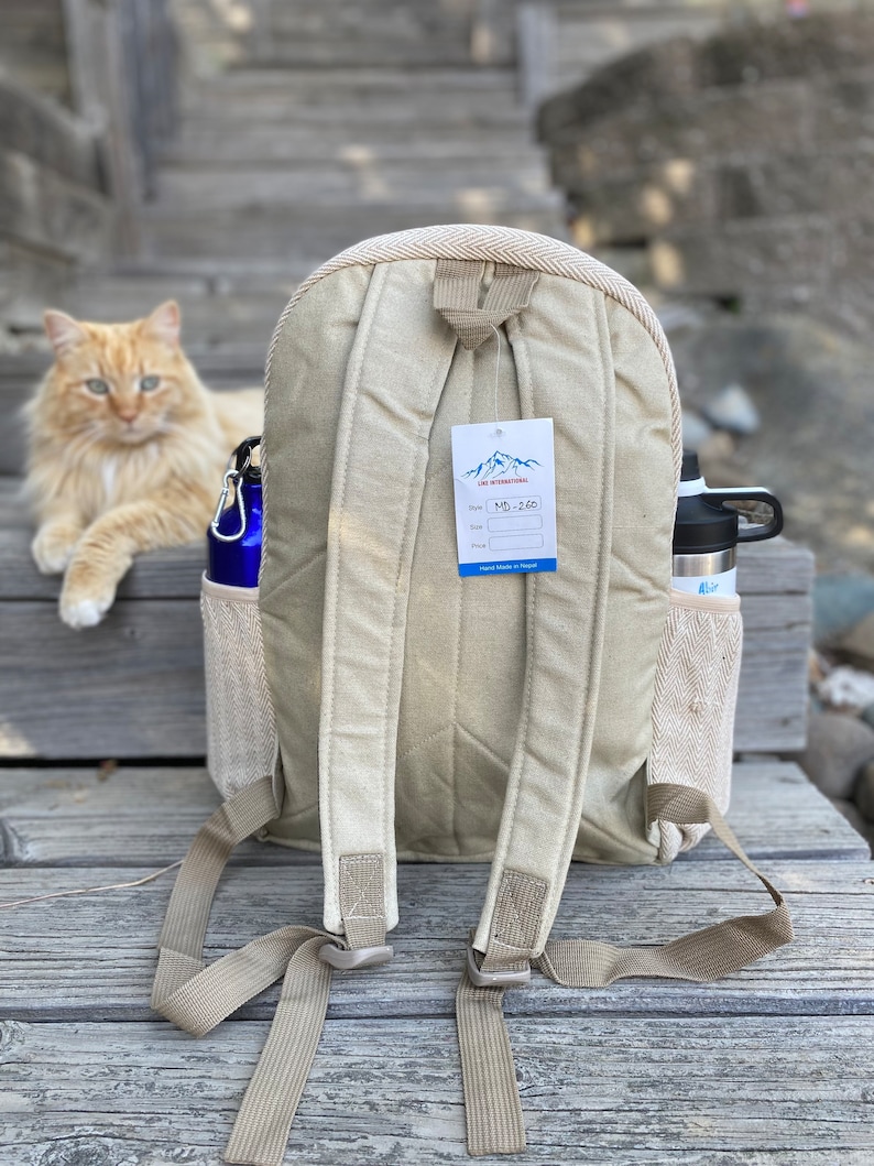 May include: A beige canvas backpack with adjustable straps. The backpack has a mesh pocket on the side and a tag that says "L&S International" and "MD-260".