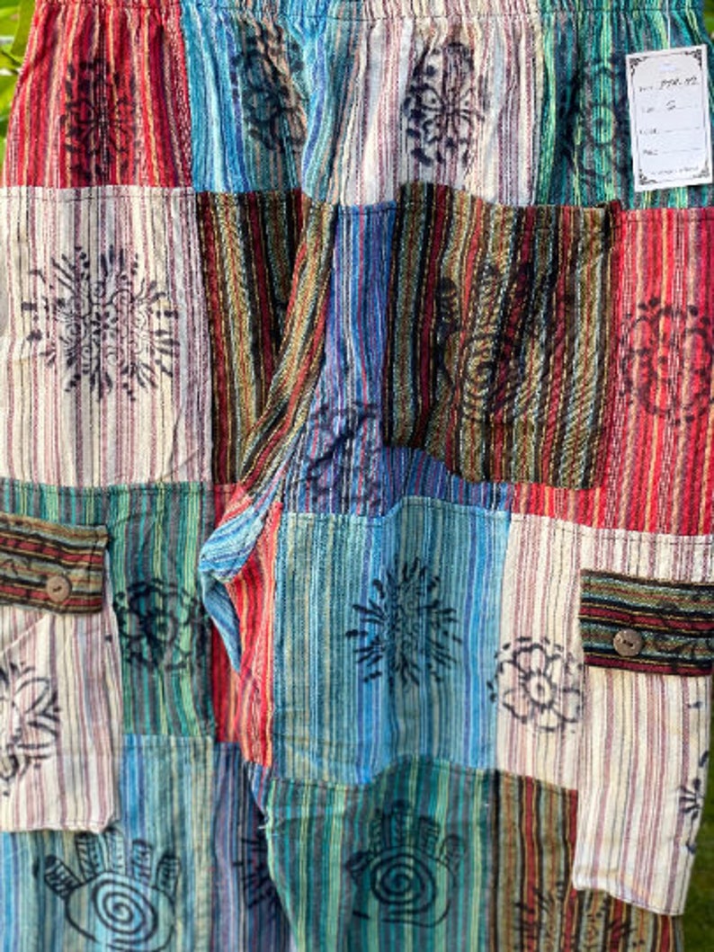 May include: Patchwork pants with a variety of colorful stripes and floral patterns. The pants have two pockets on the front.