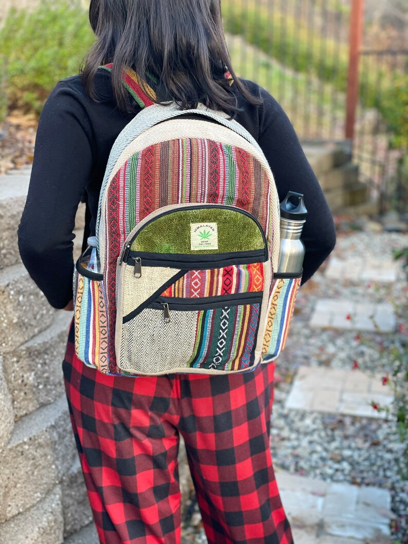 May include: A multi-coloured hemp backpack with a green patch that says "Hemp Love The Tree" and a zipped pocket. The backpack is being worn by a person wearing red and black checked trousers.