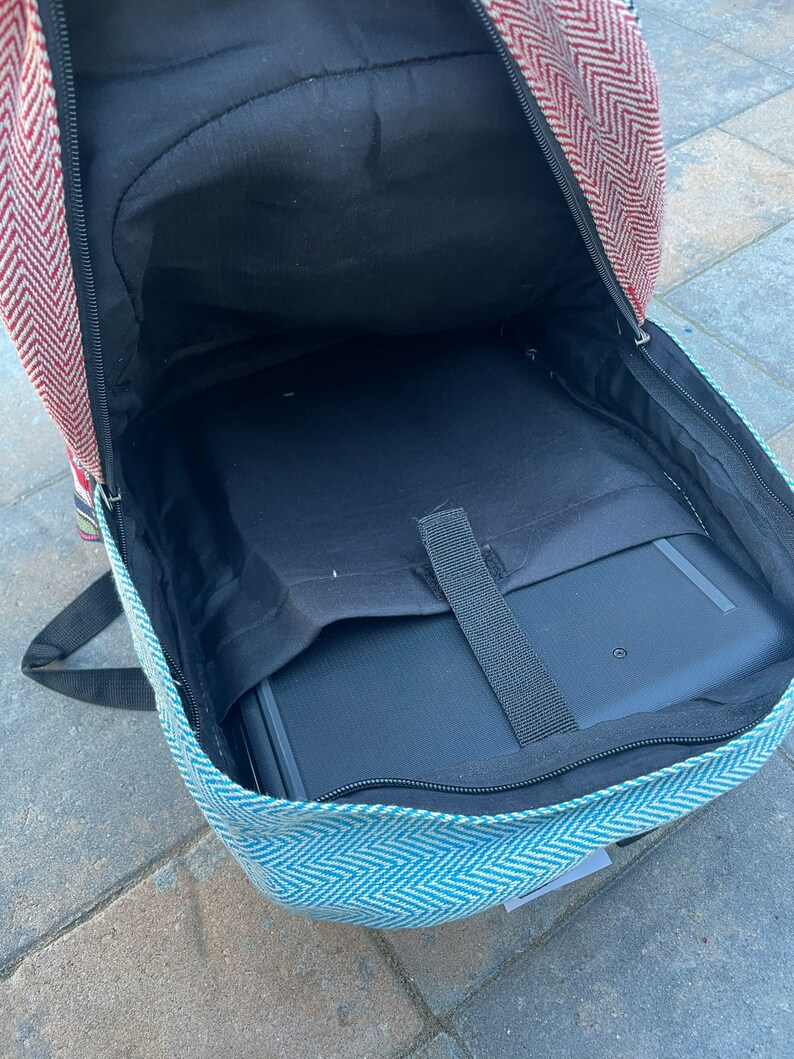 May include: A blue and white patterned backpack with a red and white chevron pattern on the top flap. The backpack is open and a black laptop is inside.
