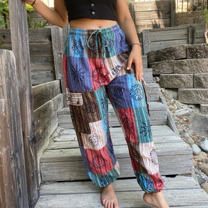 May include: Patchwork pants with a colorful, geometric pattern featuring flowers and suns. The pants have a drawstring waist and a relaxed fit.