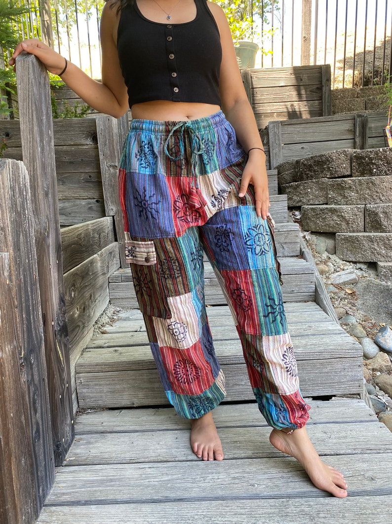 May include: Patchwork pants with a colorful, geometric pattern featuring flowers and suns. The pants have a drawstring waist and a relaxed fit.