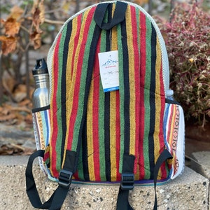 May include: A striped backpack with red, yellow, green and black stripes. The backpack has a white tag with the text "The Himalayan" and "MD-114". The backpack has black adjustable straps.