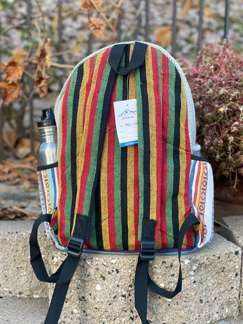 May include: A striped backpack with red, yellow, green and black stripes. The backpack has a white tag with the text "The Himalayan" and "MD-114". The backpack has black adjustable straps.