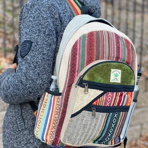 May include: A multi-coloured hemp backpack with a green patch that says "Himalayan Hemp" and a marijuana leaf logo. The backpack has a zipped pocket on the front and two side pockets.