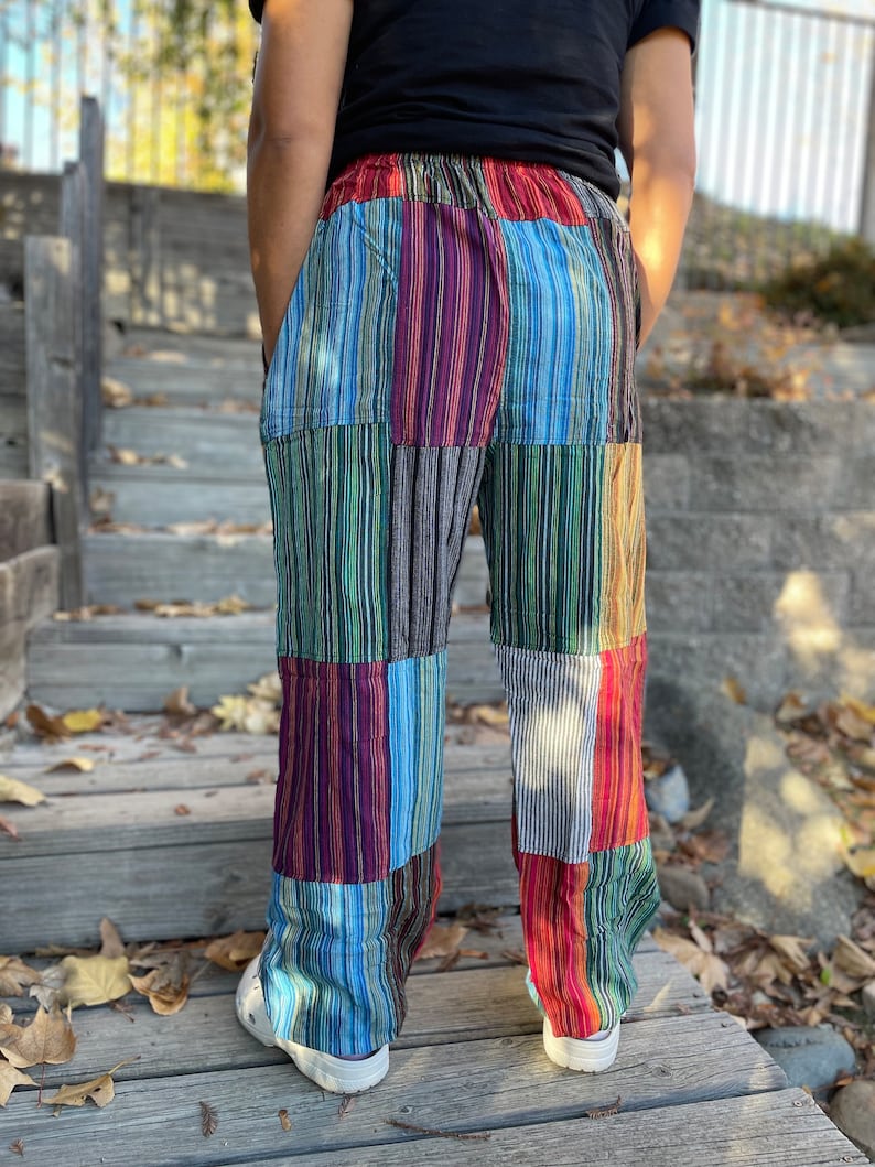 May include: Patchwork pants with a colorful striped pattern in shades of red, blue, green, and brown. The pants have a wide leg and a relaxed fit.