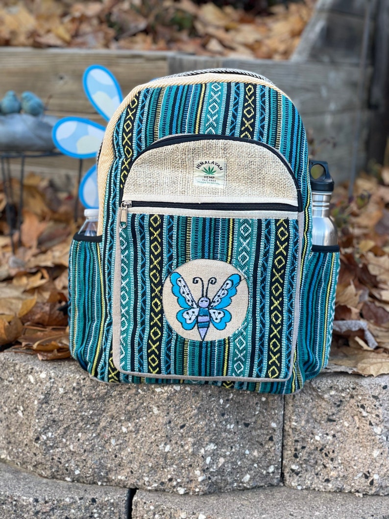 May include: A blue and white striped hemp backpack with a butterfly embroidered on the front. The backpack has a zippered pocket and a small label that reads "Himalayan Hemp Eco-Friendly".