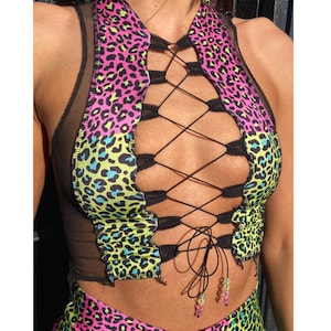 Può includere: Un top corto in mesh nero con lacci sul davanti e un motivo leopardato rosa, verde e blu.