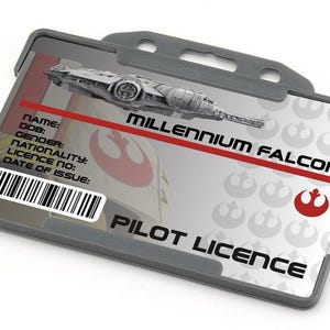 Peut inclure: Un porte-carte d'identité en plastique gris avec une carte blanche à l'intérieur. La carte comporte un code-barres noir et blanc, un symbole de l'Alliance rebelle rouge et blanc, et le texte "MILLENNIUM FALCON PILOT LICENCE".